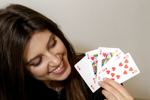Beautiful long-haired Russian indoor girl holding a Royal flush in hearts. A royal flush is the highest possible hand in poker.