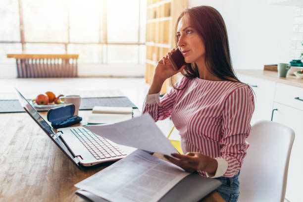 istock Thoughtful woman talking on mobile phone, while working with laptop from her home office 924450898