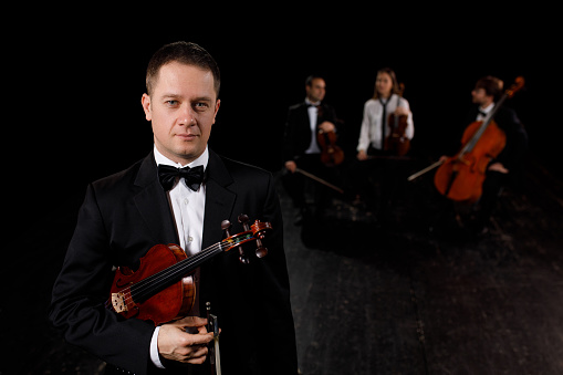 Young male violin player holding violin. The rest of string quartet in in the background.