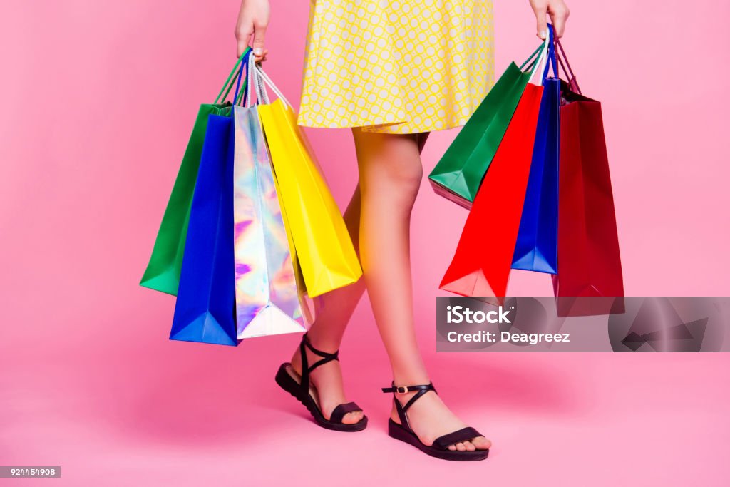 Cropped portrait of woman's slim sexy legs going from shopping having a lot of colorful bags in hands isolated on pink background, day of big sales Shopping Bag Stock Photo