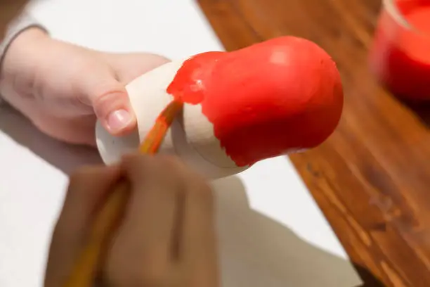 Photo of little girl paints russian nesting doll called matrioshka with red paint