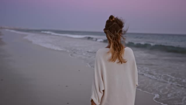 SLO MO Woman walking along a beach at dusk