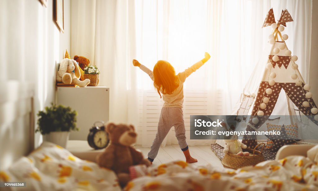 child girl wakes up  and stretches in morning in bed and stretches child girl wakes up in morning in bed and stretches by window Child Stock Photo