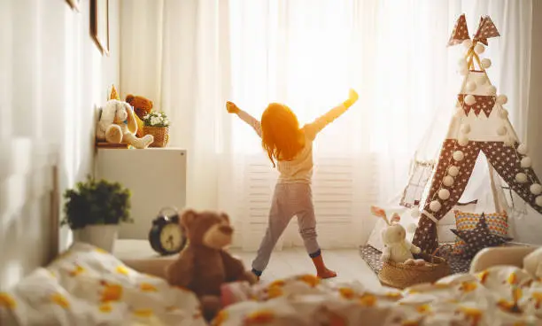 Photo of child girl wakes up  and stretches in morning in bed and stretches