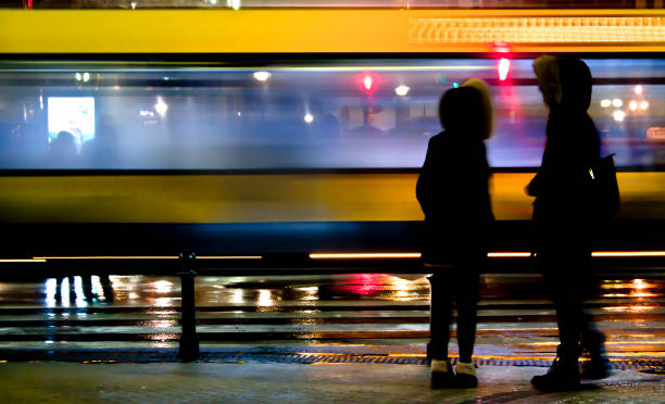 Two people waiting to cross the city street in rainy night Blurry people waiting to cross the city street in rainy night and a bus passing by in motion blur couple driving at night stock pictures, royalty-free photos & images