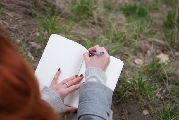 istock Redhead girl sitting on green spring grass writing in notebook. 924467760