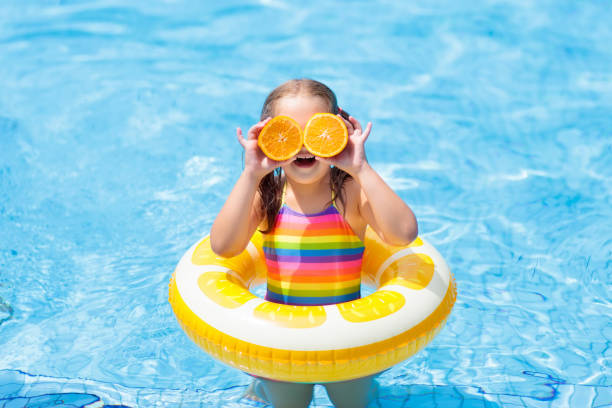 Child in swimming pool. Kid eating orange. Little girl in swimming pool with inflatable toy ring eating orange. Kids swim on summer vacation. Tropical fruit and healthy snack. Swim aids for child.  Kid on colorful float. Beach and water fun. inflatable photos stock pictures, royalty-free photos & images