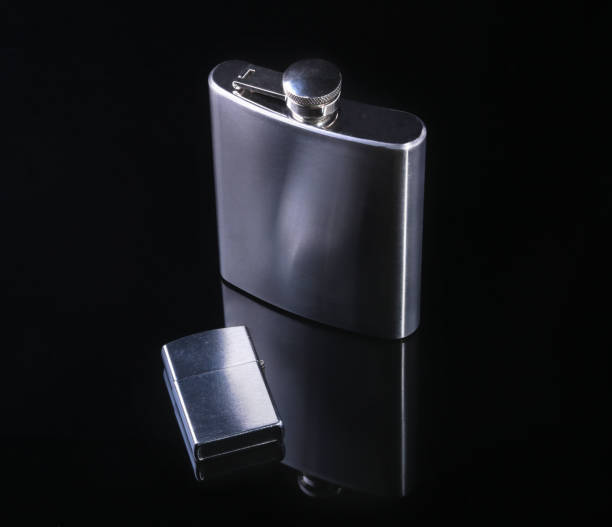 istock Stainless hip flask and lighter isolated on mirror black background. 924483594