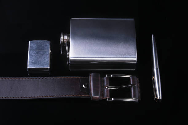 istock Stainless hip flask, lighter, pen and luxury belt isolated on mirror black background. 924483834