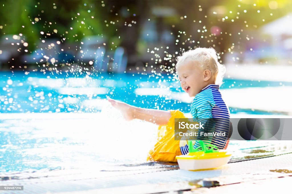 Baby in swimming pool. Family summer vacation. Baby with toy boat in swimming pool. Little boy learning to swim in outdoor pool of tropical resort. Swimming with kids. Healthy sport activity for children. Sun protection swim wear. Water toys. Child Stock Photo