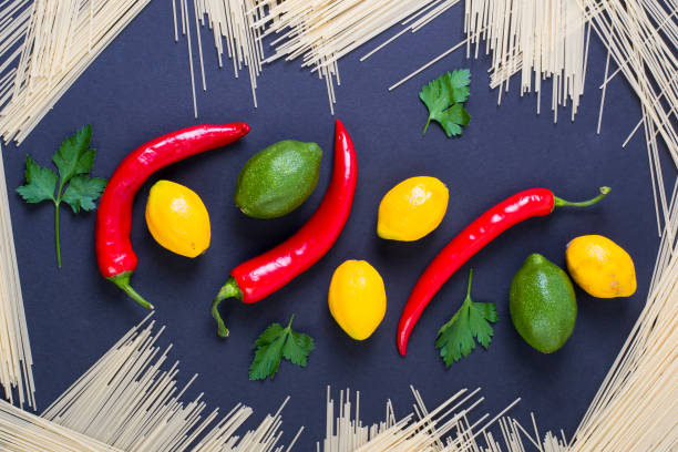 istock Bitter pepper with lime and lemon on a black background. Pasta with bitter pepper and lemon. Lemon and lime with pasta on a black background. Top view of pasta with lemon and red pepper. 924491012