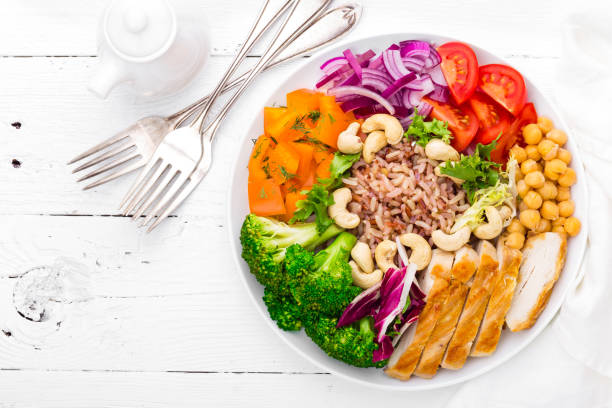 buddha bowl dish with chicken fillet, brown rice, pepper, tomato, broccoli, onion, chickpea, fresh lettuce salad, cashew and walnuts. healthy balanced eating. top view. white background - eat well plate imagens e fotografias de stock