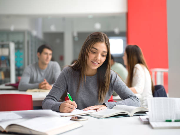istock Portrait of pretty female student at the library reading a book and taking notes using a pen and notebook 924498356