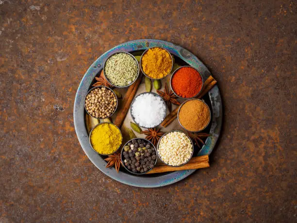 Photo of Mix spices on round metal plate - coriander seeds, ground red pepper, salt, black pepper, rosemary, turmeric, curry. Top view, close up, metall rusty background.