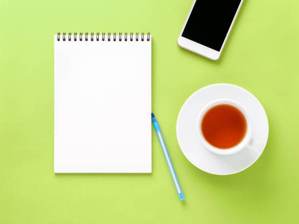 istock Top view of modern bright green office desktop with blank notepad, cup of tea, smartphone. Mock up, empty space 924499632
