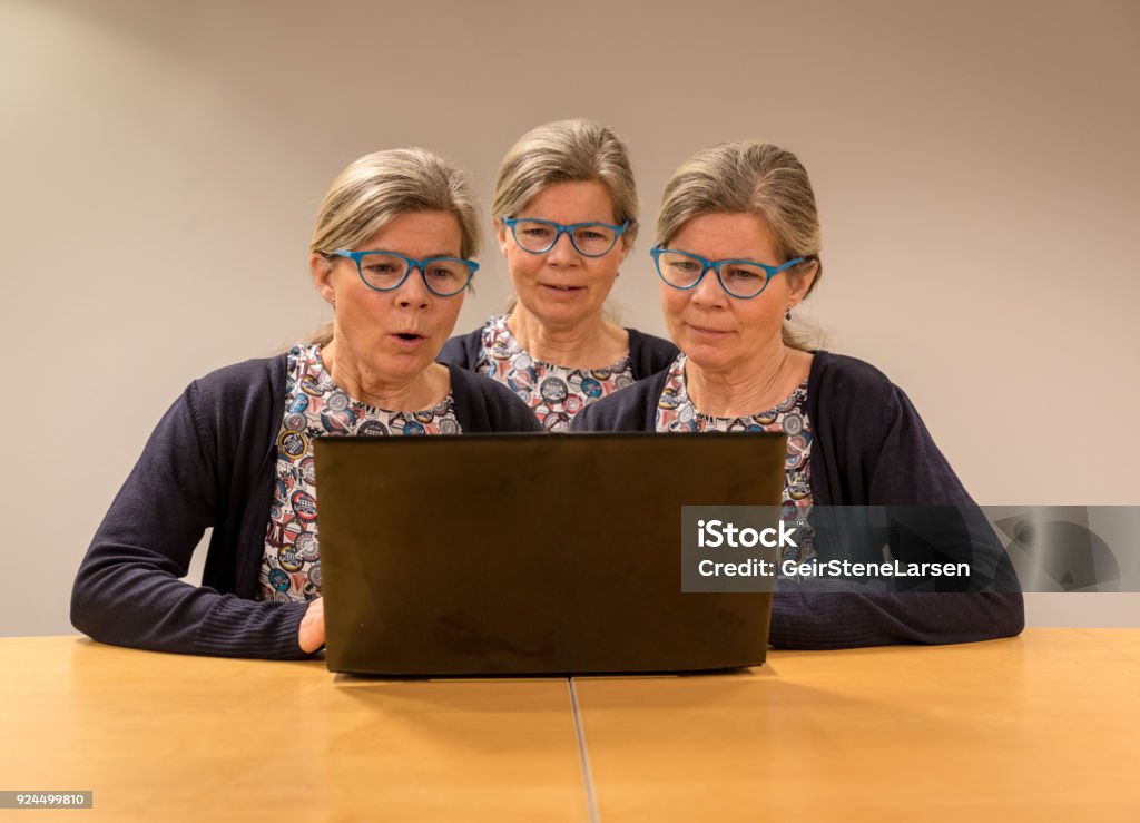 Three clones of one woman with glasses working with a pc. Oslo, Norway - February 17, 2018: Three clones og one elderly women working with a pc showing different facial expressions. Triplet - Multiple Birth Stock Photo