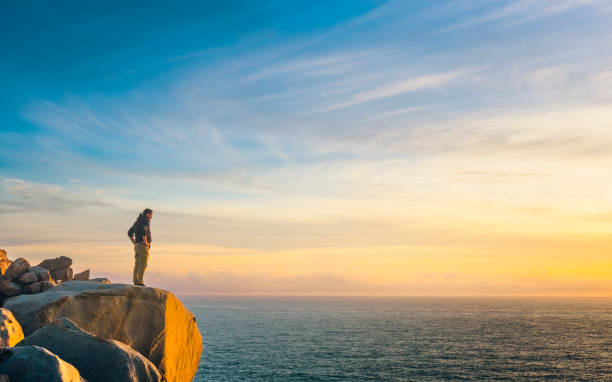 Man standing on cliff looking to sea.