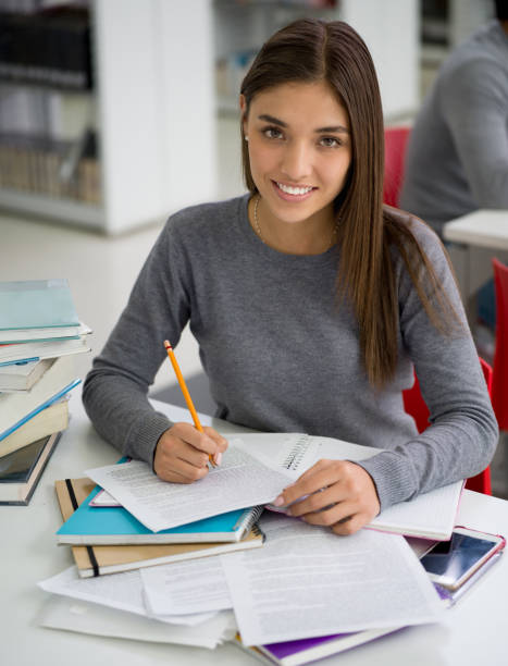istock Beautiful latin american female student at the library studying looking at camera smiling while taking notes on her notebook 924504856
