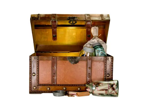 Old chest with money in rollers, bag and jar on white