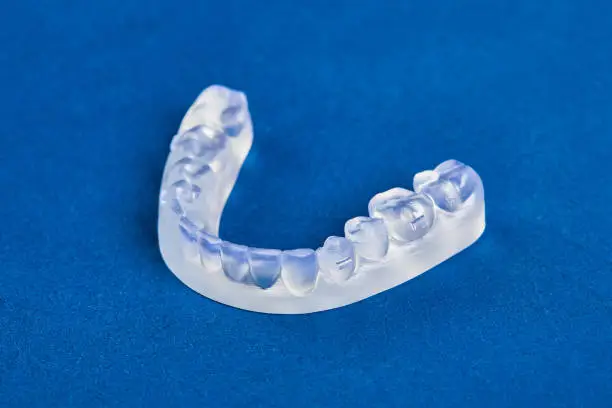 Pre-orthodontic dental trainer alignment appliance on blue background, closeup
