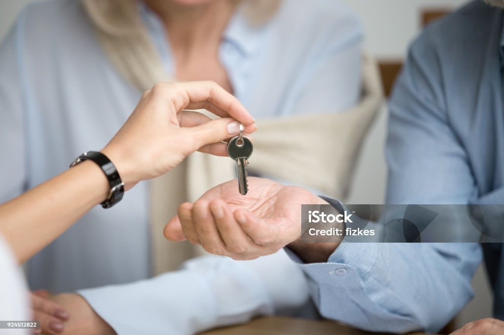 Couple of homeowners getting key to new house from Real Estate Agent Couple of homeowners getting key to new house apartment from Real Estate Agent, happy real estate owners make purchase deal, family mortgage investment and buying property concept, close up view of hands Selling Stock Photo