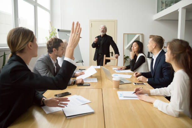 imprenditrice che alza la mano facendo domande all'allenatore senior durante la riunione di squadra - seminar asking business meeting foto e immagini stock