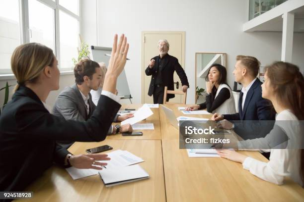 Businesswoman Raising Hand Asking Senior Coach Questions At Team Meeting Stock Photo - Download Image Now