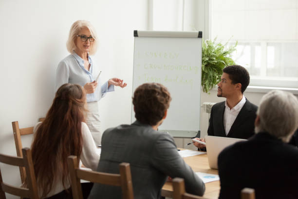 aged attractive businesswoman giving presentation at corporate team meeting - leadership business women senior adult imagens e fotografias de stock