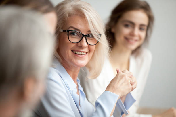 smiling aged businesswoman looking listening to colleague at team meeting - leadership business women senior adult imagens e fotografias de stock