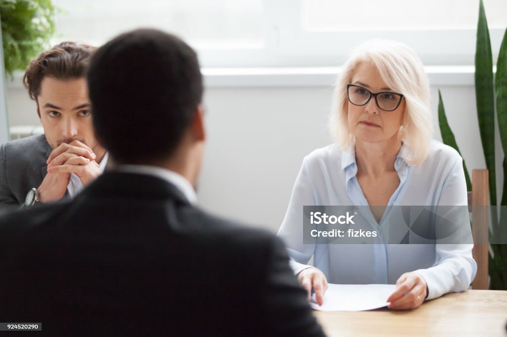 Serious attentive senior hr listening to candidate at job interview Serious attentive senior female hr manager employer listening to candidate at job interview, focused strict mature businesswoman thinking about hiring decision at difficult group negotiations concept Serious Stock Photo