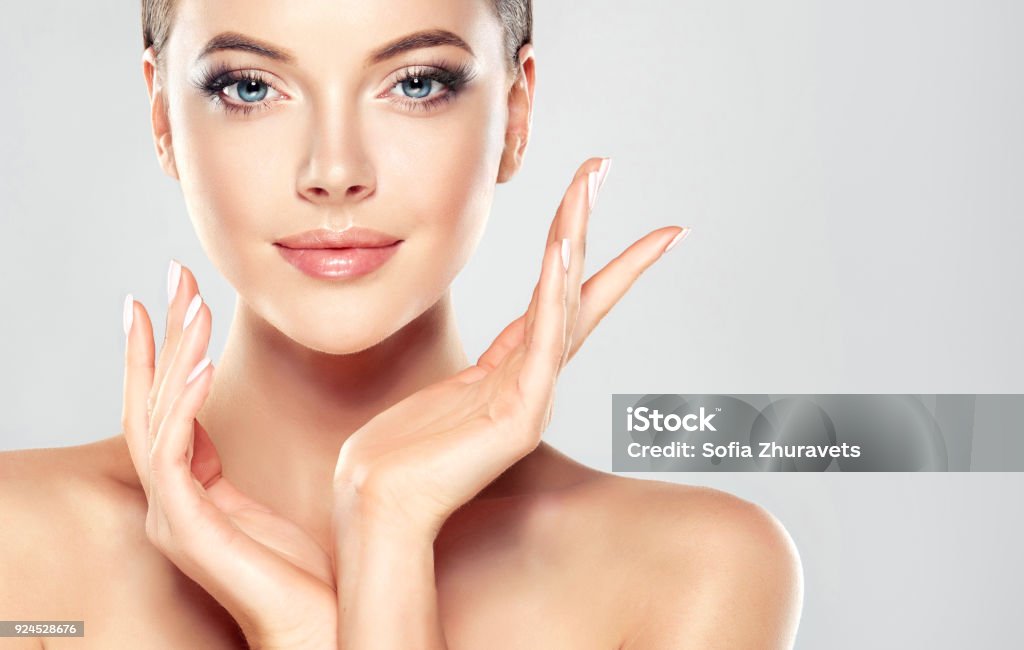 Gorgeous, young woman with clean, fresh skin is touching own face.  Light smile on the perfect face. Cosmetology. Gorgeous, young, brown haired woman with clean fresh skin is touching the face.  Light smile on the perfect face. Facial treatment, cosmetology, beauty technologies and spa. Human Face Stock Photo