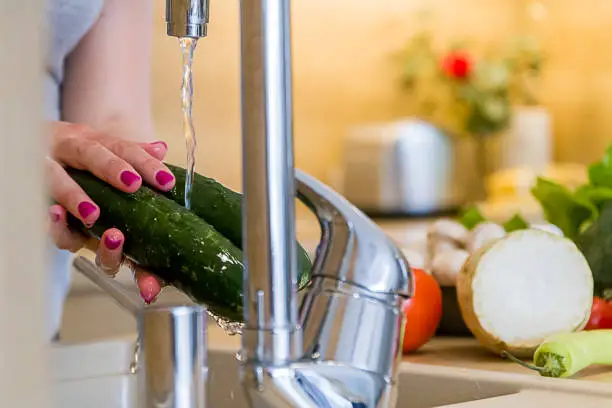 Women washing cucumber for salad - fresh vegetables concept. Fresh vegetables splashing in water before cooking. Shower to protect it from bacteria