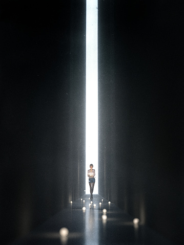 Young woman in a dark, narrow corridor, walking towards the unknown. She is holding a bunch of lit lightbulbs in her arms