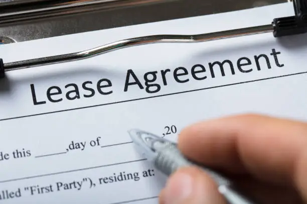 Close-up Of A Human Hand Filling Lease Agreement Form With Pen