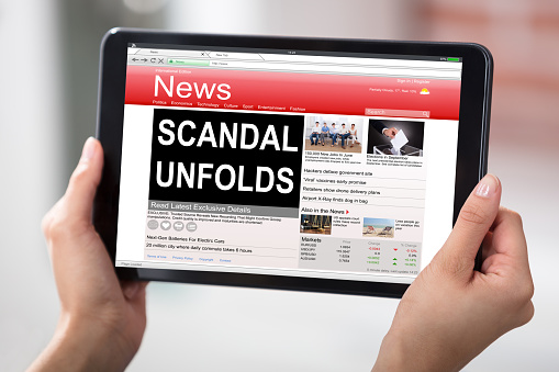 Hands Holding A Digital Table With A Screen Showing Unfolds Scandal News