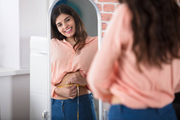 happy woman measuring waist with a tape - torso women jeans abdomen imagens e fotografias de stock