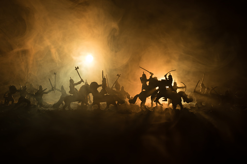 Escena de batalla medieval con caballería e infantería. Siluetas de figuras como objetos separados, lucha entre guerreros en fondo brumoso entonado oscuro. Escena de la noche. photo