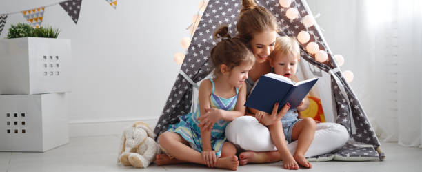 mère de famille lecture de livre pour enfants dans la tente à la maison - baby book toddler reading photos et images de collection