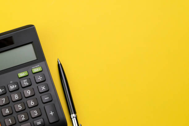 空白のコピー スペース、数学、コスト、税務、または投資計算の鮮やかな黄色の背景のテーブルの上の計算機と黒いペンのフラット レイアウトやトップ ビュー - calculations ストックフォトと画像