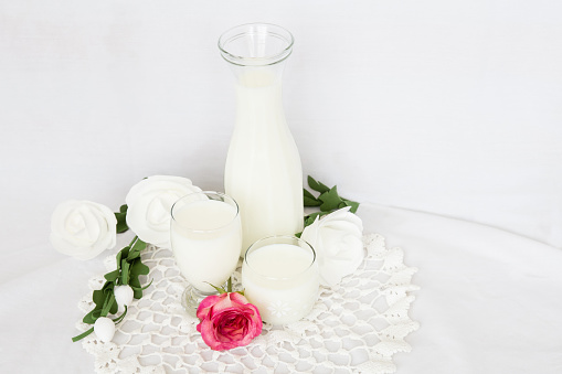 horizontal image of a tall glass jug filled with milk along with smaller glasses of milk on white background with room for copy space.
