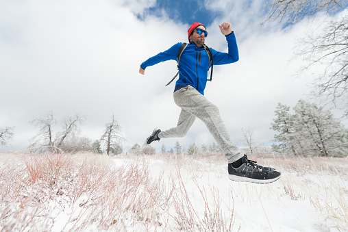 Man running in the winter through the forest.  Low angle in mid-air.