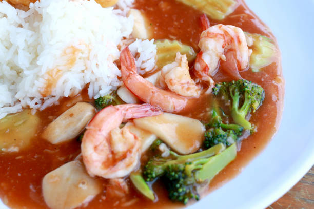 stir fried shrimp and Broccoli in thai red curry paste sauce with rice, Curry fried shrimps and cooked rice in white dish closeup on wooden table. Thai style food.