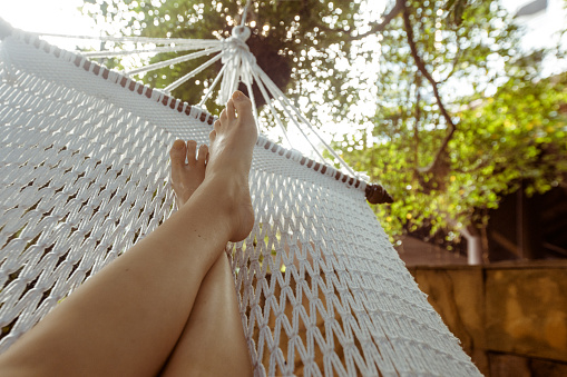 Crop shot of barefoot feet lying in white hammock and lounging in backyard.