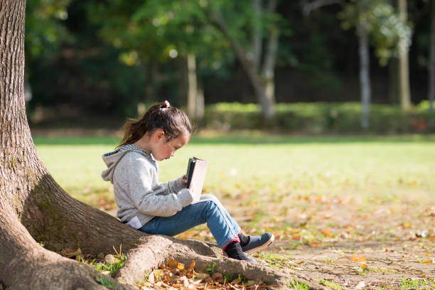 istock Little girl sitting on a tree and reading a book 924676848