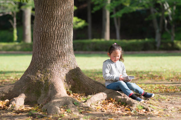 istock Little girl sitting on a tree and reading a book 924676922