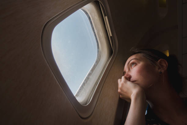 Sad woman at porthole in plane Sad girl at the porthole in the plane. Young woman on passenger seat near window in airplane expatriate photos stock pictures, royalty-free photos & images