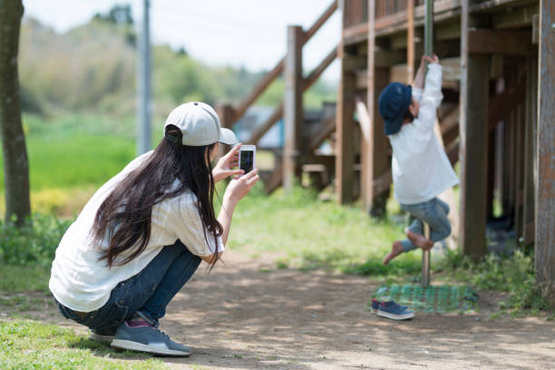 スマート フ��ォンで撮影する母、クライミングバーに挑戦する娘 - two generation family 写真 ストックフォトと画像