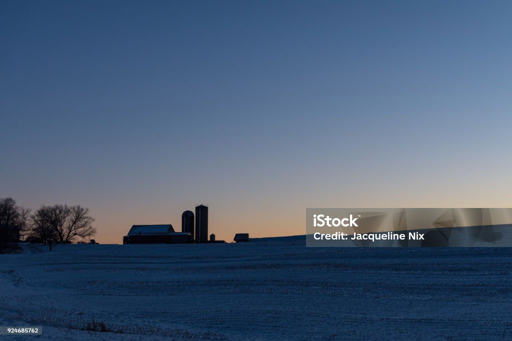 Farm background at sunrise Winter scene of a dairy barn and silos on a hilltop at sunrise with blank area above. Snow Stock Photo