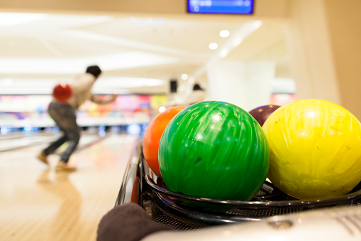 Close up photo of bowling balls while two people are playing bowling in the background.