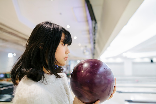 A portrait of a Japanese young woman in a bowling alley while holding a bowling ball.